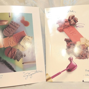 May include: Two rectangular product brochures featuring makeup imagery. The left brochure displays crushed eyeshadows, lipstick, and mascara with the text Sweet Allure and Signature. The right brochure shows pressed powder, lipstick, and a pink applicator with the text Free Spirit.