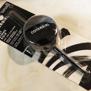May include: A black CoverGirl Just Gimme Noir gel pot eyeliner with a brush applicator. The product is packaged on a black and white striped card. The package reads "NEW NOUVEAU" and contains 2.4g (0.084 oz) of product.