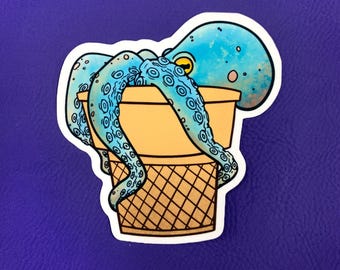 May include: A blue octopus with yellow eyes is sitting in a waffle cone ice cream cup. The octopus has a light blue body with darker blue spots and tentacles.