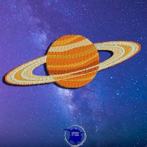 May include: A yellow and orange embroidered planet with a ring system against a dark blue background with white stars. The planet is stylized to look like Saturn.