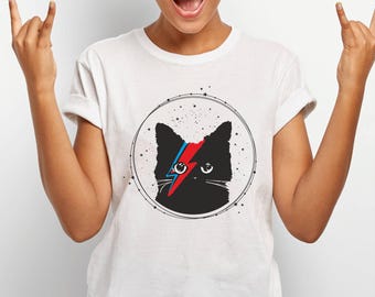 May include: White t-shirt featuring a black cat graphic with a red and blue lightning bolt design. The cat is inside a circle with stars. The shirt has short sleeves and a crew neck.