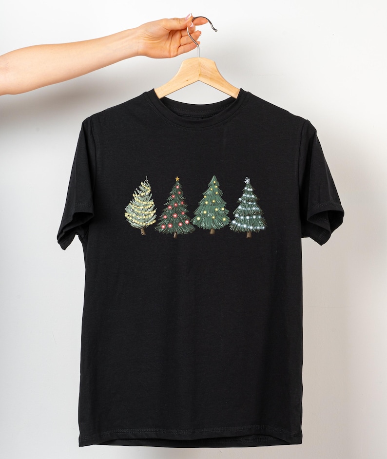May include: Black t-shirt featuring four embroidered Christmas trees. The trees are decorated with lights and ornaments in various colors, including white, red, and gold. The trees are arranged in a row across the chest of the shirt.