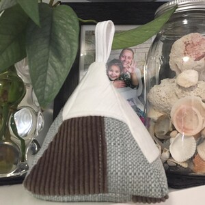 May include: A triangular doorstop with a white fabric top, brown corduroy bottom, and a light blue fabric side. The doorstop has a loop handle.