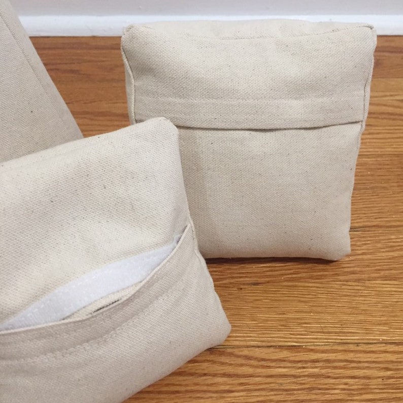 May include: Three off-white canvas pillow covers with a zipper closure. The pillow covers are made of a soft, natural fabric and have a simple, minimalist design.
