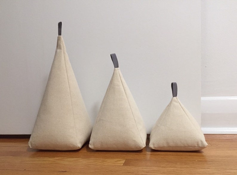 May include: Three beige fabric doorstops in different sizes with grey handles. The doorstops are arranged in a row from largest to smallest.