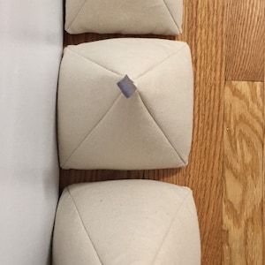 May include: Three white fabric pyramid-shaped cushions with grey fabric ties at the top.
