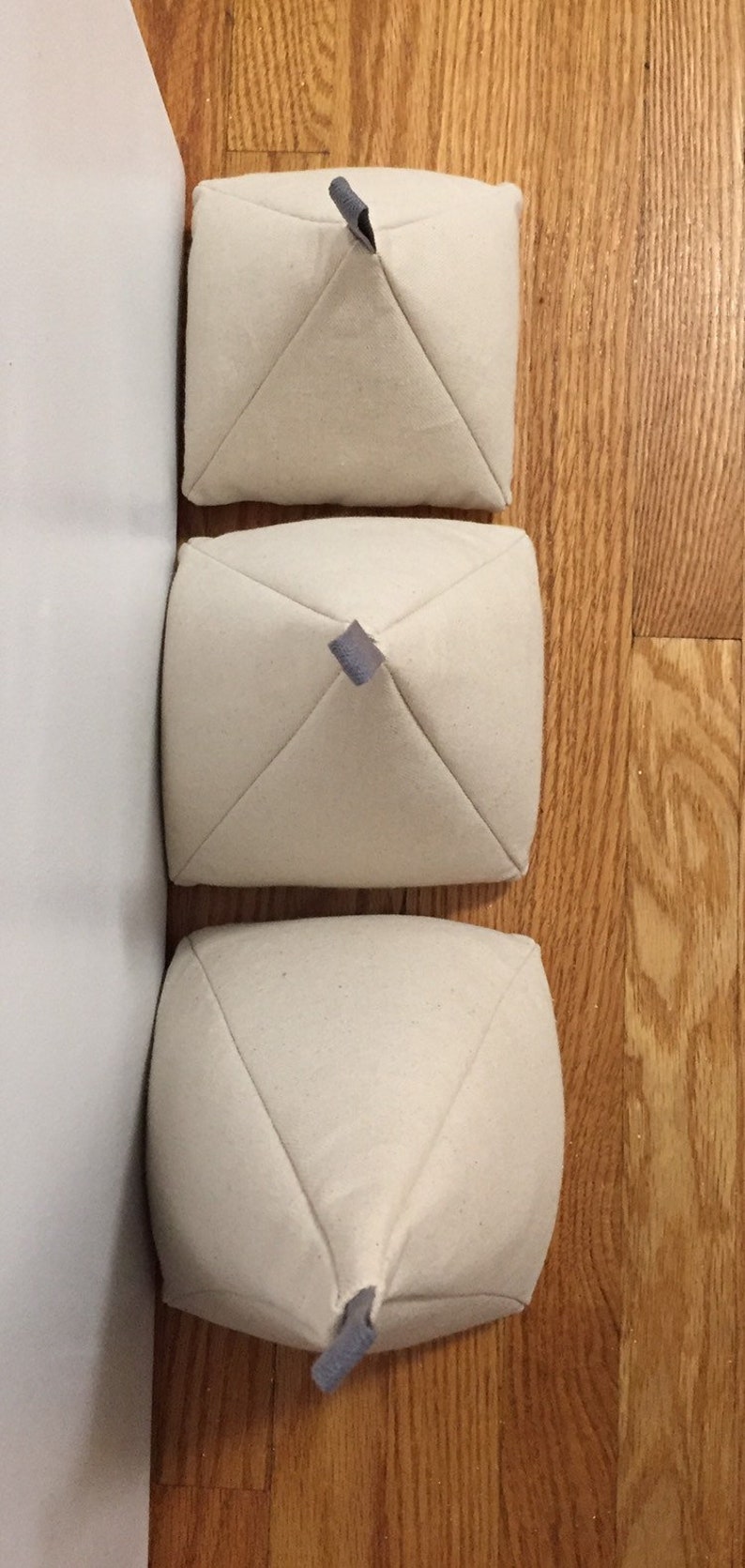 May include: Three white fabric pyramid-shaped cushions with grey fabric ties at the top.