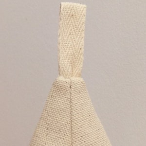 May include: A cream-coloured canvas bag with a cream-coloured fabric handle. The bag is made of a tightly woven fabric.