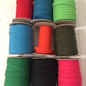 May include: Ten spools of cotton webbing in various colours, including red, blue, green, orange, black, and pink. The spools are arranged in three rows on a white surface.