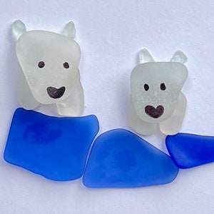 Puede incluir: Dos figuras de osos polares de vidrio marino blanco esmerilado, cada una con rasgos faciales negros y una base de vidrio marino azul. La imagen est&aacute; sobre un fondo blanco.