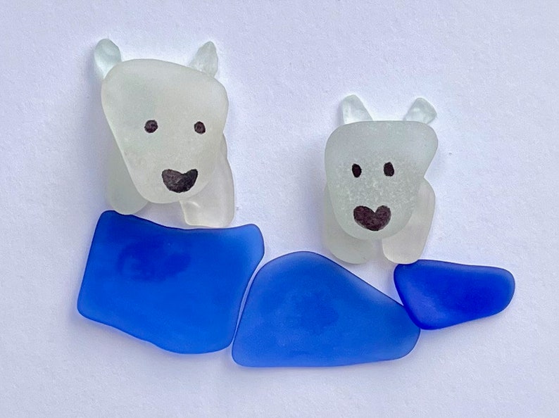 Puede incluir: Dos figuras de osos polares de vidrio marino blanco esmerilado, cada una con rasgos faciales negros y una base de vidrio marino azul. La imagen est&aacute; sobre un fondo blanco.
