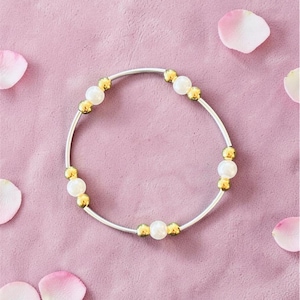 May include: A circular bracelet featuring a thin silver-toned wire band accented with alternating white spherical beads and small gold-toned metallic spheres arranged in a repeating pattern around the entire circumference of the jewelry piece.