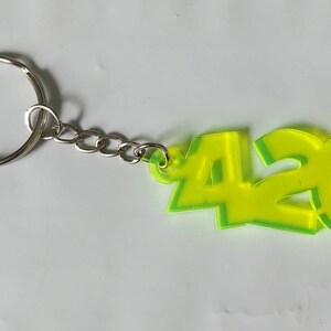 May include: A green and yellow acrylic keychain with the number 420 on it. The keychain has a silver metal ring and chain.
