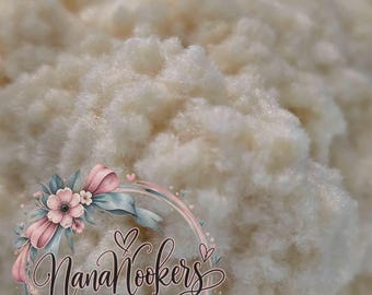 May include: A close-up view of a soft, off-white, fibrous material with a fluffy, textured appearance. Overlaid on the lower left is a circular logo featuring pink flowers, green leaves, and the text NanaNookers REBORN ART by Christy Paradee.