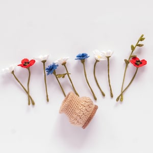 May include: A small crocheted basket with a collection of crocheted flowers in red, white, and blue. The flowers are arranged in a line, resembling a bouquet.