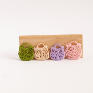 May include: Four small crocheted bags in different colors: green, beige, purple, and pink. The bags are lined up on a wooden surface.