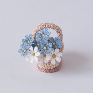 May include: A small crocheted basket filled with blue and white crocheted flowers. The basket is light pink and has a handle.