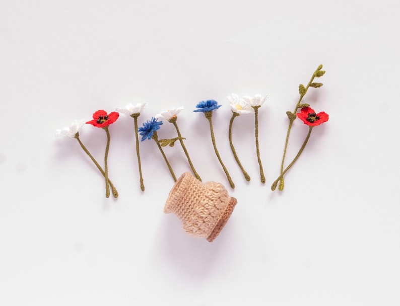 May include: A small crocheted basket with a collection of crocheted flowers in red, white, and blue. The flowers are arranged in a line, resembling a bouquet.