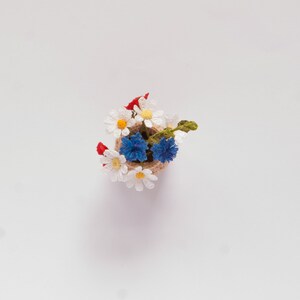 May include: A small crocheted bouquet of white daisies and blue cornflowers in a brown burlap pot.