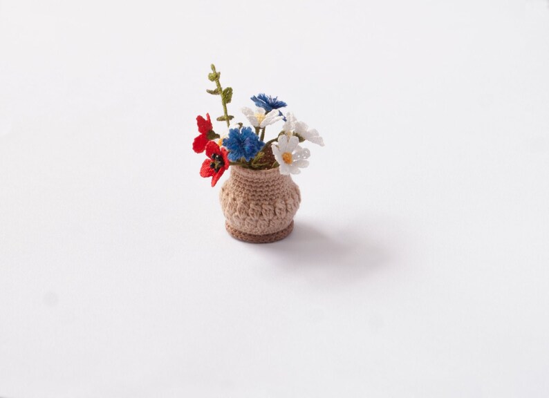 May include: A small crocheted flower arrangement in a brown pot. The flowers are white, red, and blue.