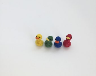 May include: Four crocheted duck figurines lined up in a row. The ducks are yellow, green, blue, and red.