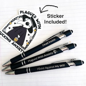 May include: Three black pens with silver accents and a white sticker featuring a plague doctor illustration. The pens are engraved with the phrases "Dead Inside", "Plagued With Anxiety", and "I Exist Against My Will".