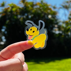 May include: A clear sticker with a yellow cartoon dog with a green collar. The dog is looking to the right and has its tongue sticking out.