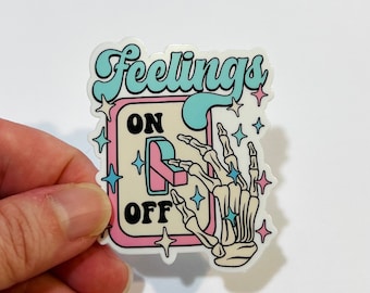 May include: A sticker with a light blue and white design featuring a skeleton hand flipping a switch labeled "ON" and "OFF". The text "Feelings" is written in a retro font above the switch.