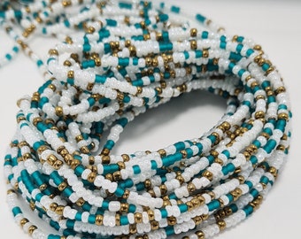 May include: A waist bead necklace made with white, teal, and gold beads. The beads are strung together in a repeating pattern.