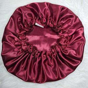 May include: A burgundy satin sleep cap with a gathered elastic band. The cap is designed to protect hair while sleeping.
