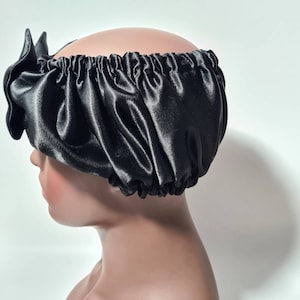 May include: A black satin sleep cap with a gathered design. The cap is worn on a mannequin head.