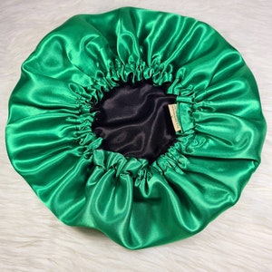 May include: A bright green satin bonnet with a black lining. The bonnet is gathered at the top and has a small tag that reads "Handmade with Love".