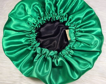 Può includere: Un berretto di raso verde brillante con fodera nera. Il berretto è raccolto nella parte superiore e ha un piccolo cartellino con la scritta "Handmade with Love".