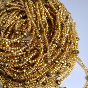 May include: A close-up of a pile of gold-coloured beads. The beads are small and round, and they are strung together in a long strand. The beads are shiny and reflective, and they have a metallic finish.
