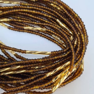 May include: A brown beaded waist beads necklace with gold spacers. The beads are small and uniform in size. The gold spacers are twisted and add a touch of elegance to the necklace.