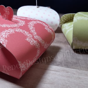 May include: Three small gift boxes with heart-shaped lids. The boxes are decorated with floral patterns and are in shades of red, green, and white.