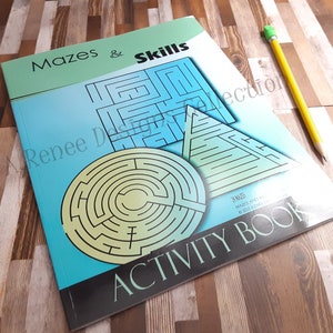 May include: An activity book titled "Mazes & Skills" with a blue and green cover featuring maze designs. A yellow pencil with a green eraser rests on the book. The book's cover displays a circular, triangular, and square maze.