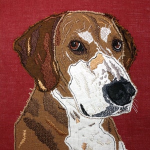May include: Embroidered portrait of a dog with brown and white fur, set against a red background. The dog's eyes are brown, and its nose is black. The embroidery has a textured appearance.