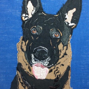 May include: Embroidered image of a German Shepherd dog with black fur and brown markings. The dog is looking directly at the viewer with its tongue sticking out. The background is a solid blue.