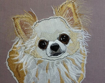 May include: Embroidered image of a white chihuahua with brown eyes and a light brown coat. The chihuahua is looking directly at the viewer. The embroidery is done on a light brown fabric.