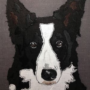 Pode incluir: Um cão border collie preto e branco com manchas marrons nas orelhas, bordado em um fundo de tecido cinza.