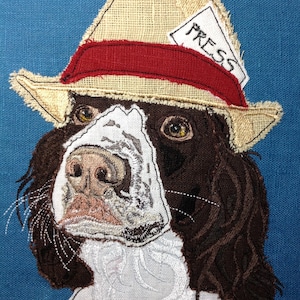 May include: Embroidered image of a brown and white dog wearing a tan and red hat with a white label that says "PRESS".