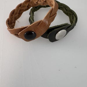 Peut inclure: Deux bracelets en cuir tressés avec des fermoirs à pression. Un bracelet est marron et l'autre est vert.