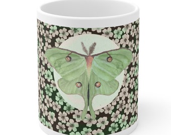 May include: White ceramic mug with a green and brown floral pattern. A green luna moth is centered on the mug, surrounded by a white circle.