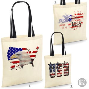 Könnte beinhalten: Drei Tragetaschen mit verschiedenen Designs der amerikanischen Flagge. Die erste Tasche zeigt einen Weißkopfseeadler mit der amerikanischen Flagge in Form der Vereinigten Staaten. Die zweite Tasche hat eine Palme mit der amerikanischen Flagge im Hintergrund. Die dritte Tasche hat das Wort "USA" in großen Buchstaben mit einem abgenutzten Design der amerikanischen Flagge.