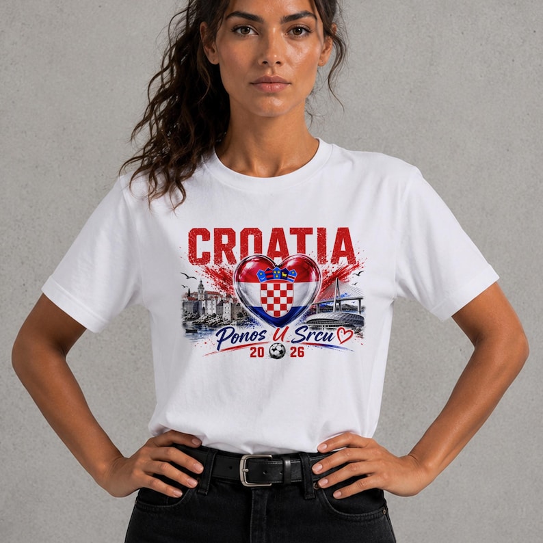 Może przedstawiać: Biały t-shirt z nadrukiem graficznym zawierającym napis CROATIA, chorwacką flagę w kształcie serca oraz napis Ponos U Srcu 20 26. Wz&oacute;r zawiera ilustracje nadmorskich budynk&oacute;w, mostu oraz grafikę przedstawiającą piłkę nożną.