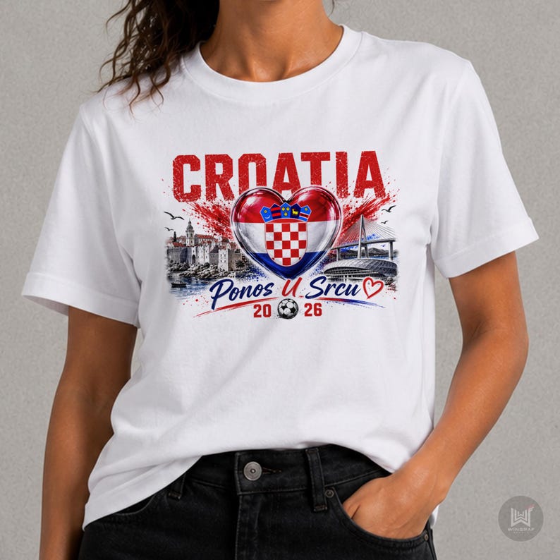 Może przedstawiać: Biały t-shirt z kr&oacute;tkim rękawem z nadrukiem graficznym zawierającym napis CROATIA nad chorwacką flagą w kształcie serca. Pod sercem znajduje się napis Ponos U Srcu, piłka nożna oraz liczby 20 i 26 umieszczone po obu stronach piłki.