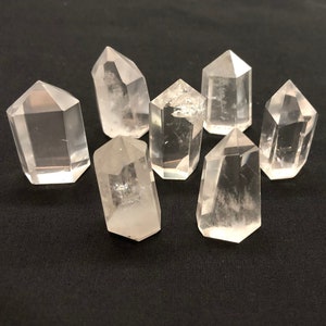 Może przedstawiać: Osiem przezroczystych punktów kryształu kwarcowego, znanych również jako kryształy kwarcowe z podwójną końcówką, na czarnym tle.