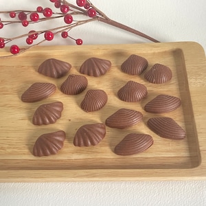 May include: A wooden tray with 15 chocolate seashells arranged in a pattern. The seashells are a dark brown colour and have a smooth, glossy finish.