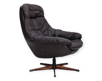 May include: A dark brown leather lounge chair with a high back and tufted cushioning. The chair features a swivel base with a central black metal column connected to a four-pointed star-shaped wooden base with a distinct dark wood grain pattern.